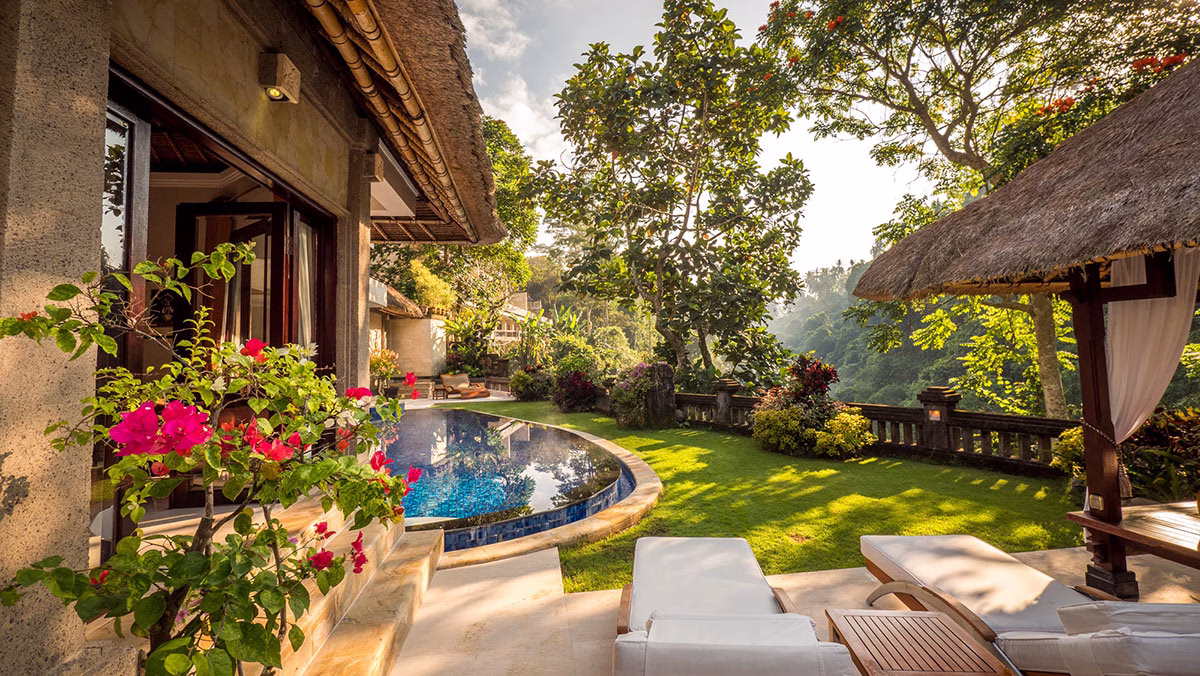 Der sonnendurchflutete Außenbereich der Viceroy Villa mit einem geschwungenen, blauen Infinity-Pool, weißen Sonnenliegen, einer gemütlichen Lounge-Bale und farbenfrohen Bougainvillea-Blüten im Vordergrund
