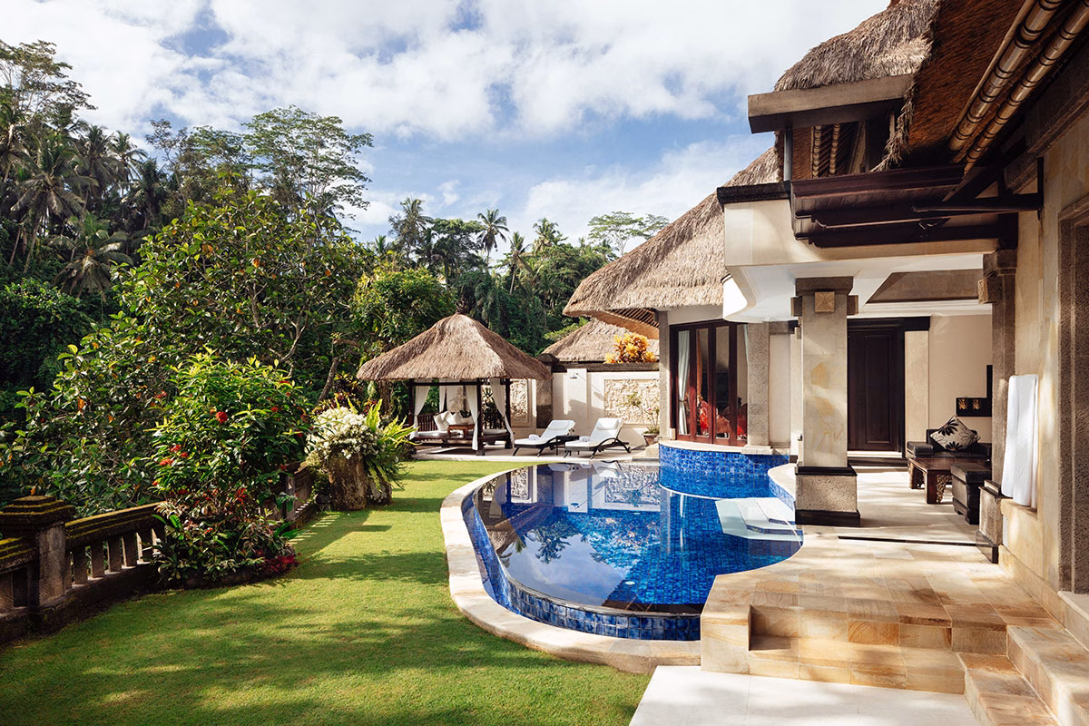 Blick auf die weitläufige Garten- und Poolterrasse der Viceroy Villa mit einem halbrunden Infinity-Pool, einem traditionellen Pavillon im Hintergrund und einer eleganten Architektur unter balinesischen Reetdächern