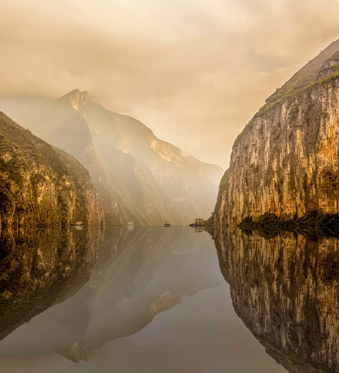 Landschaft am Jangtsekiang in China. Die Szenerie ist geprägt von steilen Klippen und Bergen, die sich im ruhigen Wasser spiegeln.