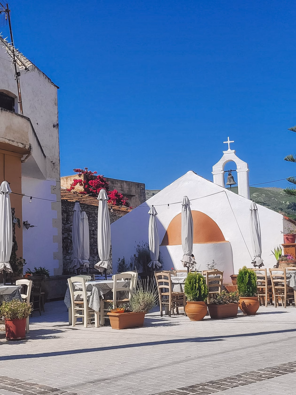 Uriger Stadtgern mit weißer Kirche und Restaurant mit Terrasse in einem kleinen Ort auf Kreta