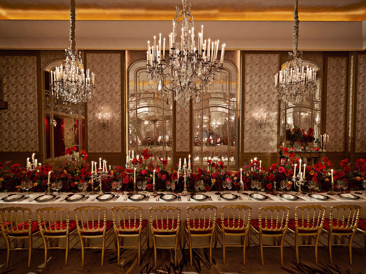 Eine extrem lange, prachtvoll eingedeckte Festtafel im Salon Haute Couture für ein exklusives Dinner, dekoriert mit hunderten roten Rosen, silbernen Kandelabern, Kristallkronleuchtern und goldenen Stühlen vor verspiegelten Wänden