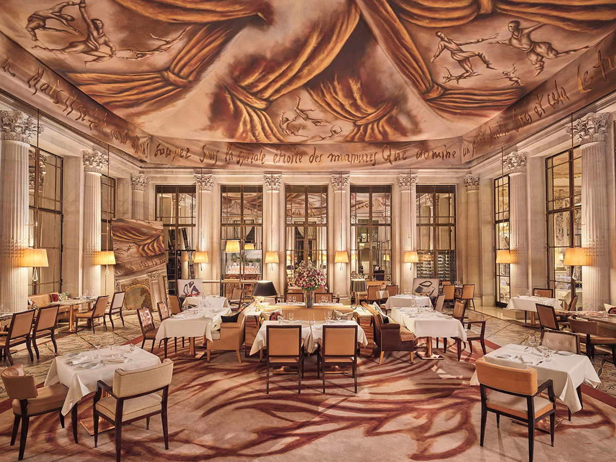 Das kunstvolle Restaurant Le Dalí im Le Meurice mit einer monumentalen, surrealistisch bemalten Deckenbespannung, eleganten weißen Tischen, modernen Polstersesseln und raumhohen Spiegelwänden