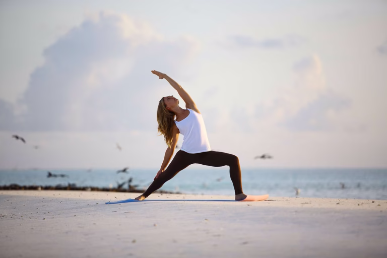 Frau macht Yoga am Strand im andBeyond Mnemba Island